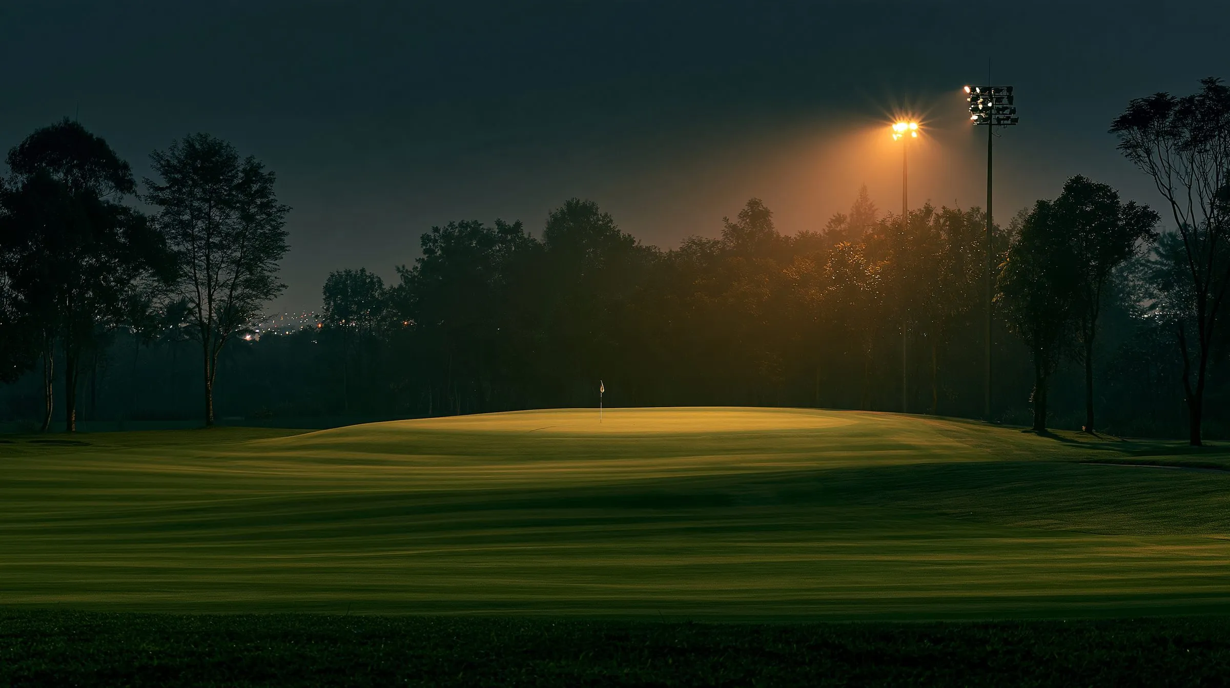 A floodlit fairway at night, the green glowing under the lights